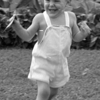 Young child in overalls running on a lawn.