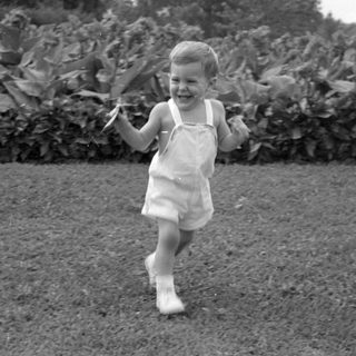 Young child in overalls running on a lawn.