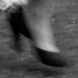 Child in white overalls running near a woman.
