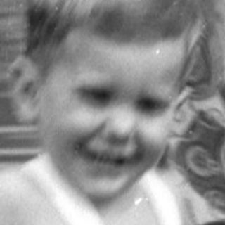 Child in white overalls running near a woman.