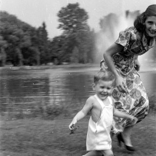 Child in white overalls running near a woman.