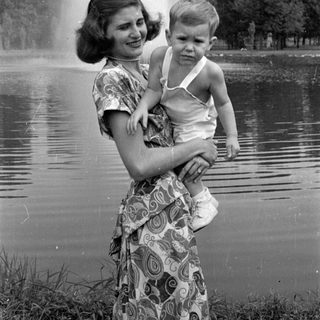 Woman holding a child by a pond fountain.