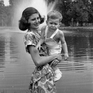 Woman holding a child by a pond fountain.