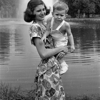 Woman holding a child by a pond fountain.