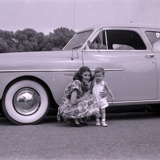 Woman and child posing beside a vintage sedan.