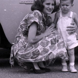 Woman and child posing beside a vintage sedan.