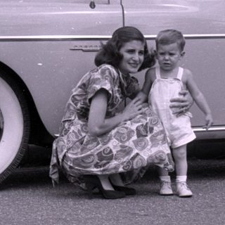 Woman and child posing beside a vintage sedan.