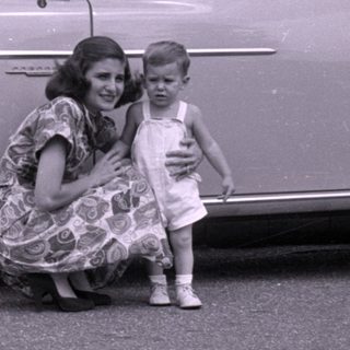 Woman and child posing beside a vintage sedan.