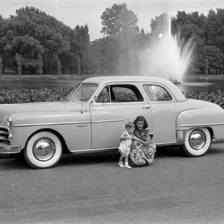 Woman and child posing beside a vintage sedan.