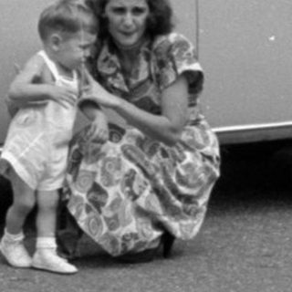 Woman and child posing beside a vintage sedan.