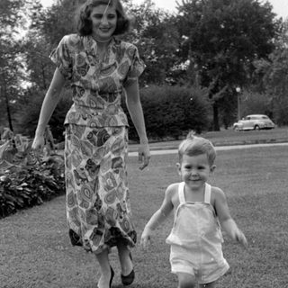 Woman and child walking on a grass lawn.