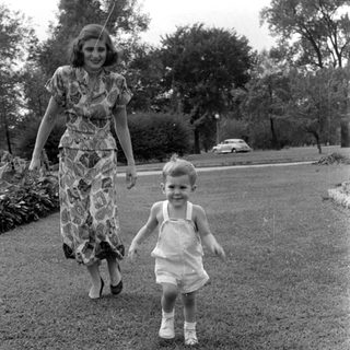 Woman and child walking on a grass lawn.