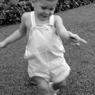 Young child in overalls walking on a lawn.