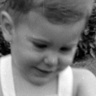 Young child in overalls walking on a lawn.