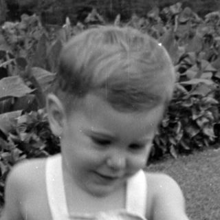 Young child in overalls walking on a lawn.