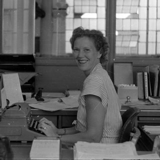 Woman at a typewriter in a mid-century office.