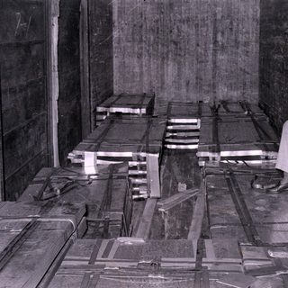Man sitting beside strapped crates in wooden interior.