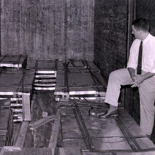 Man sitting beside strapped crates in wooden interior.