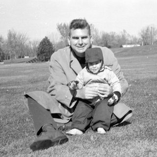 Man and child sitting on a grassy hill.