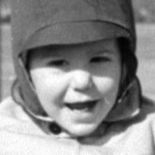 Child in winter clothes standing in a grassy field.