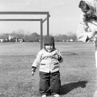 Child in winter clothes standing in a grassy field.
