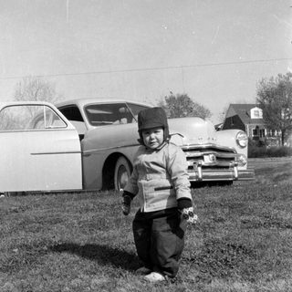 Child in winter clothes standing before a vintage car.