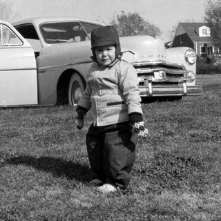 Child in winter clothes standing before a vintage car.