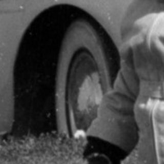 Child in winter clothes standing before a vintage car.