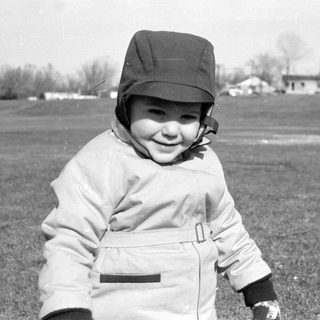 Child in a hat standing in a grassy field.
