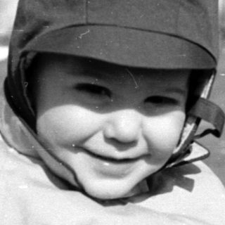 Child in a hat standing in a grassy field.