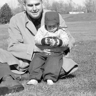 Man and small child sitting in a grassy field.