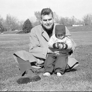 Man and small child sitting in a grassy field.