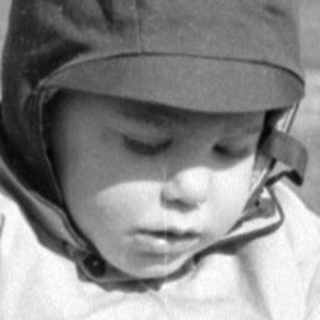 Child in winter clothes holding stones in a field.