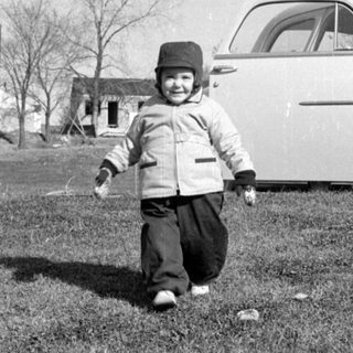Child walking in yard near vintage car.