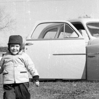 Child walking in yard near vintage car.