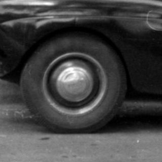 Woman holding a child in front of a vintage car.
