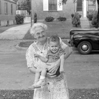 Woman holding a child in front of a vintage car.