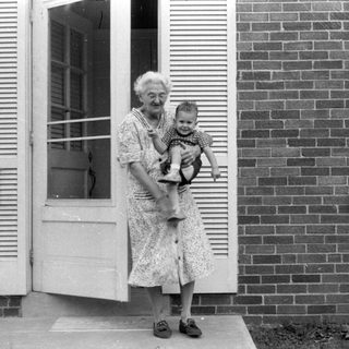 Woman holding a child in a brick house doorway.