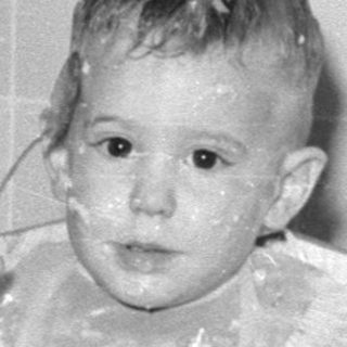 Toddler in high chair with food on face.
