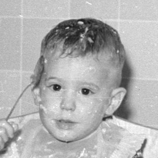 Toddler in high chair with food on face.