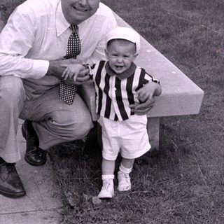 Man and child in striped shirt by concrete bench.