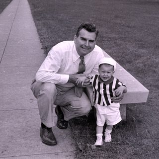 Man and child in striped shirt by concrete bench.