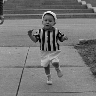 Child in striped shirt walking before large building.