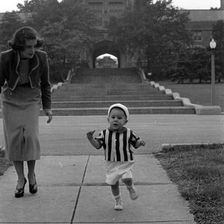 Child in striped shirt walking before large building.