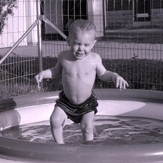 Child standing in an inflatable pool in a yard.