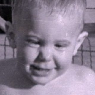 Child standing in an inflatable pool in a yard.