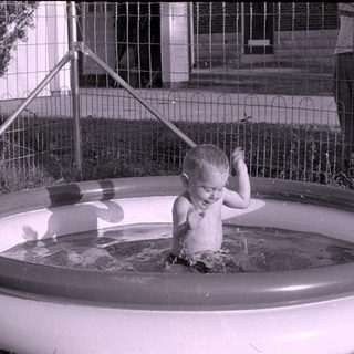 Child playing in an inflatable pool outdoors.