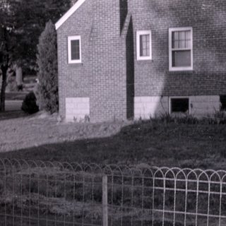 Older woman holding a baby in a residential yard.
