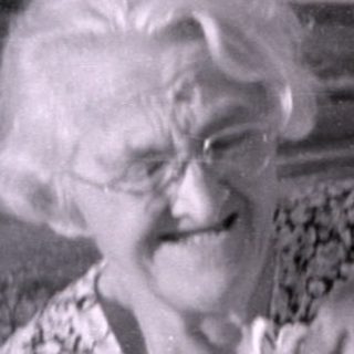 Older woman holding a baby in a residential yard.
