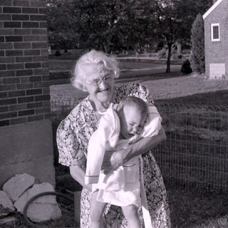 Older woman holding a baby in a residential yard.